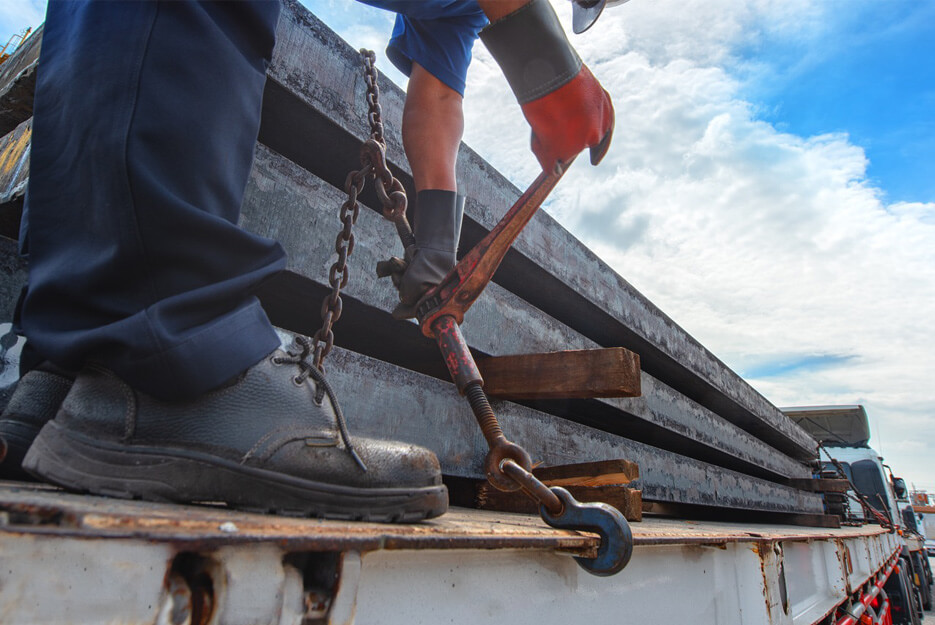 Worker securing steel bars to a truck using chains and turnbuckles